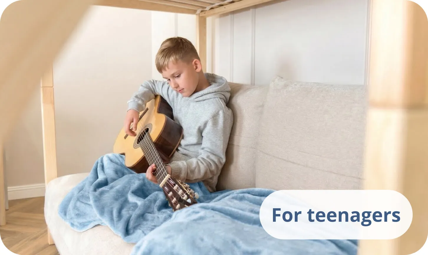 Teenager playing an acoustic guitar on a bed covered with a blue blanket.
